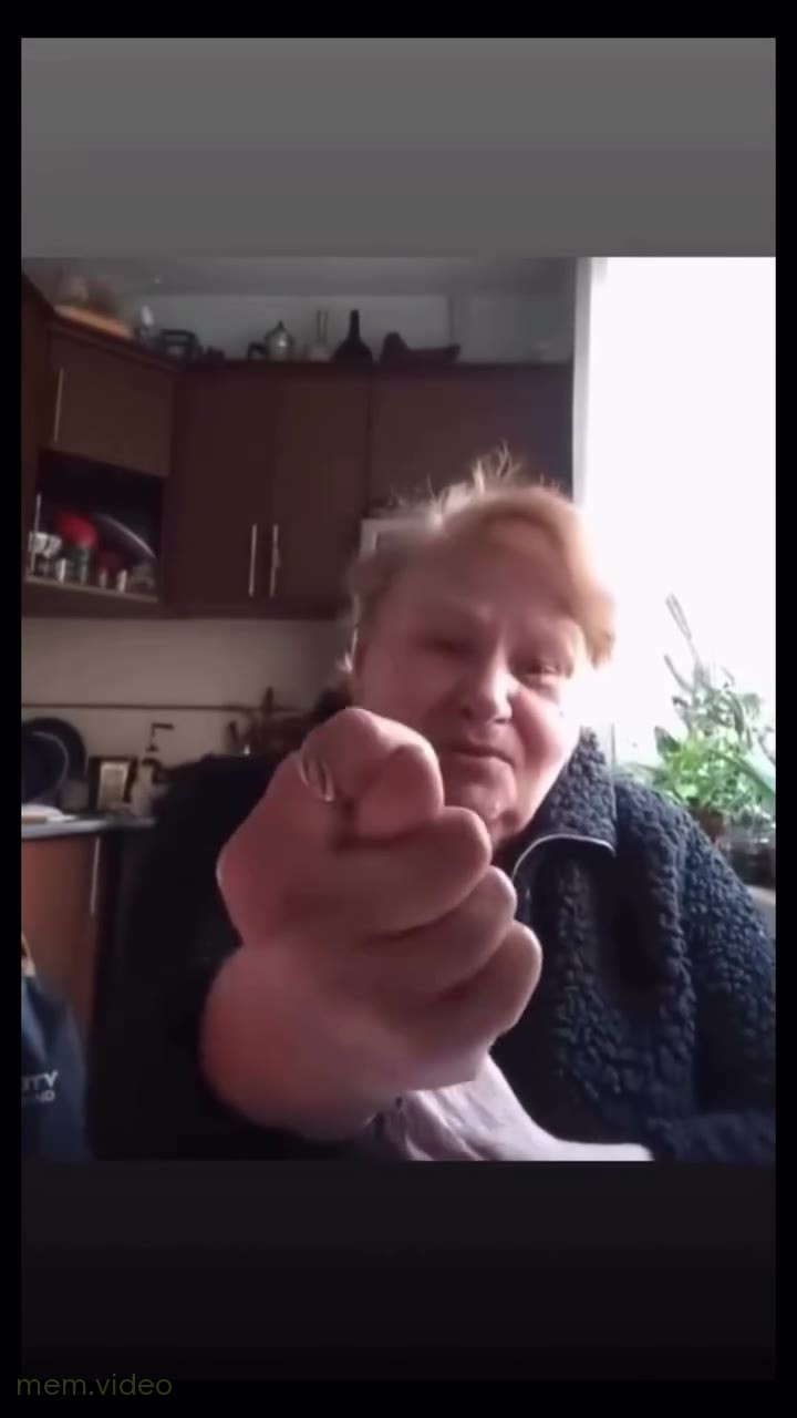 Кадр: Бабушка сидит на кухне и показывает средний палец и кукиш