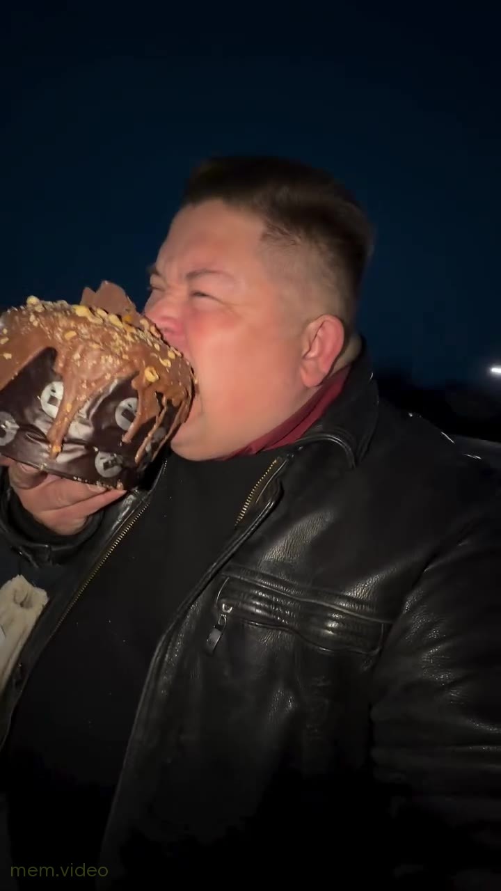 Кадр: Мужчина в кожаной куртке ест огромный кекс на улице