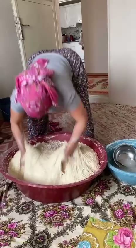 Кадр: Женщина в розовом платке месит тесто в огромном тазу