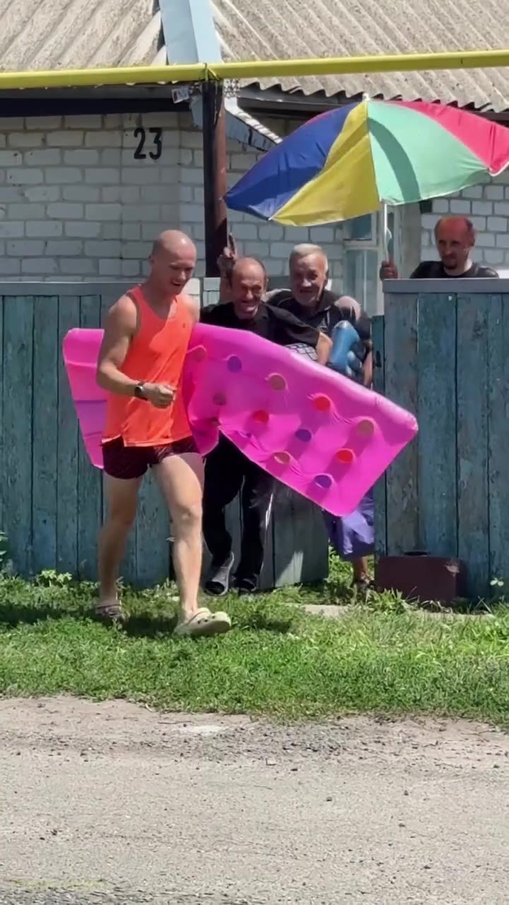 Кадр: Мужчина в оранжевой майке с матрасом танцует у забора