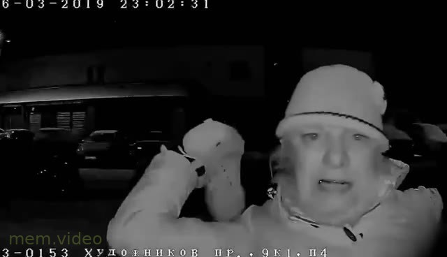 Кадр: Женщина в шапке ругается и бьет в камеру домофона